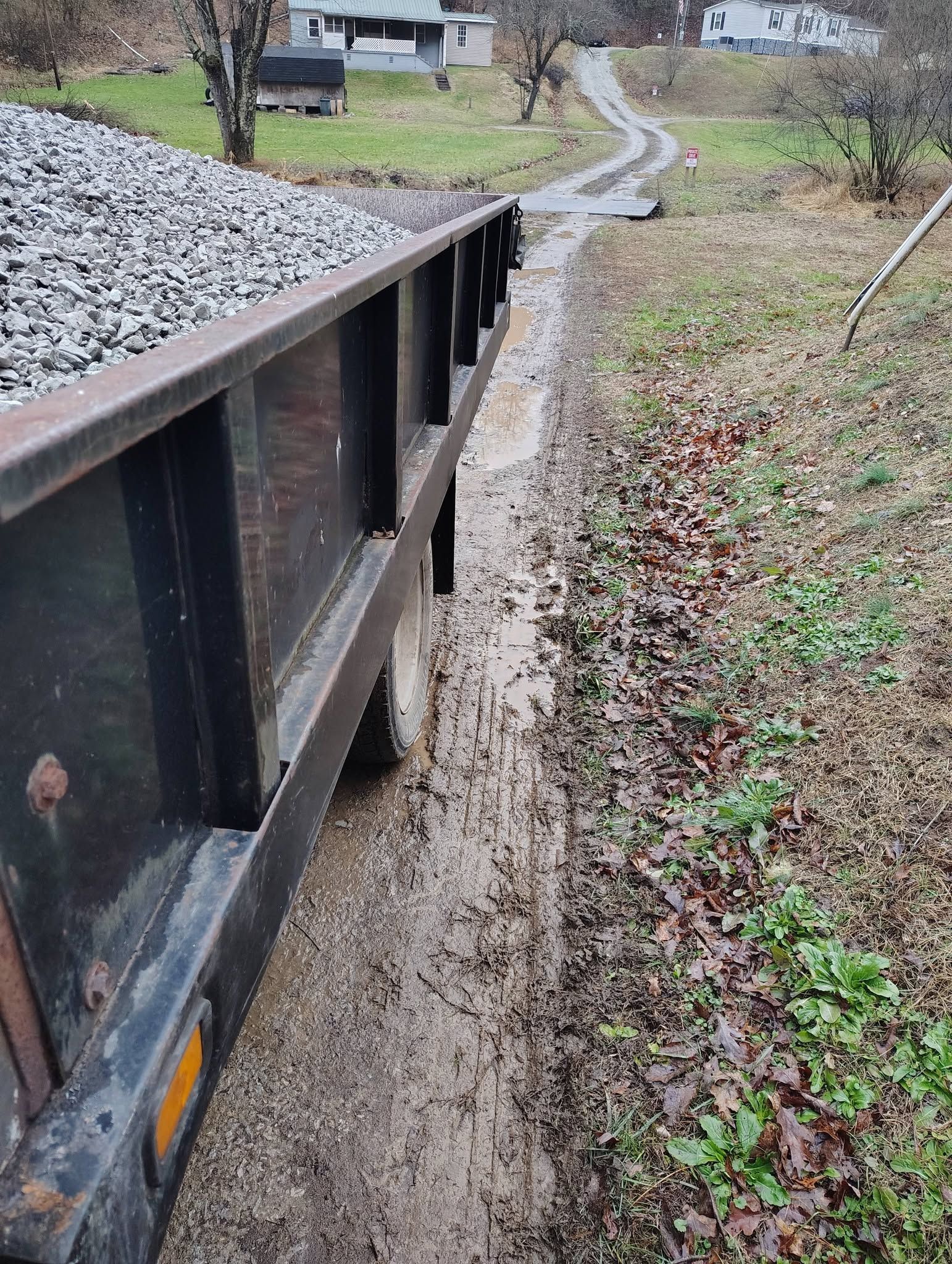 Metal dumpster along a muddy rural path beside gravel and a grassy slope