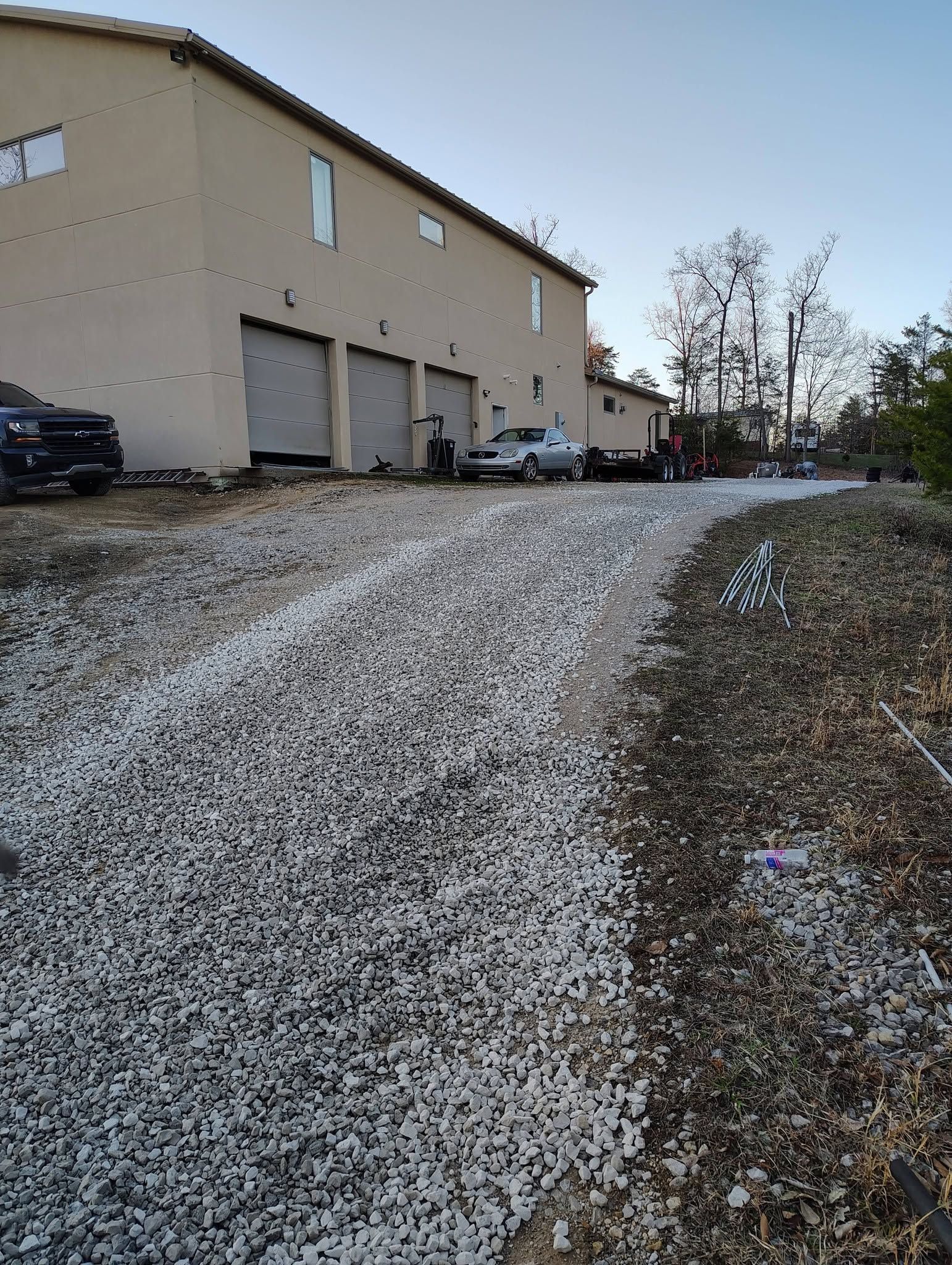 Snow-dusted gravel driveway beside beige building and parked cars under a clear sky