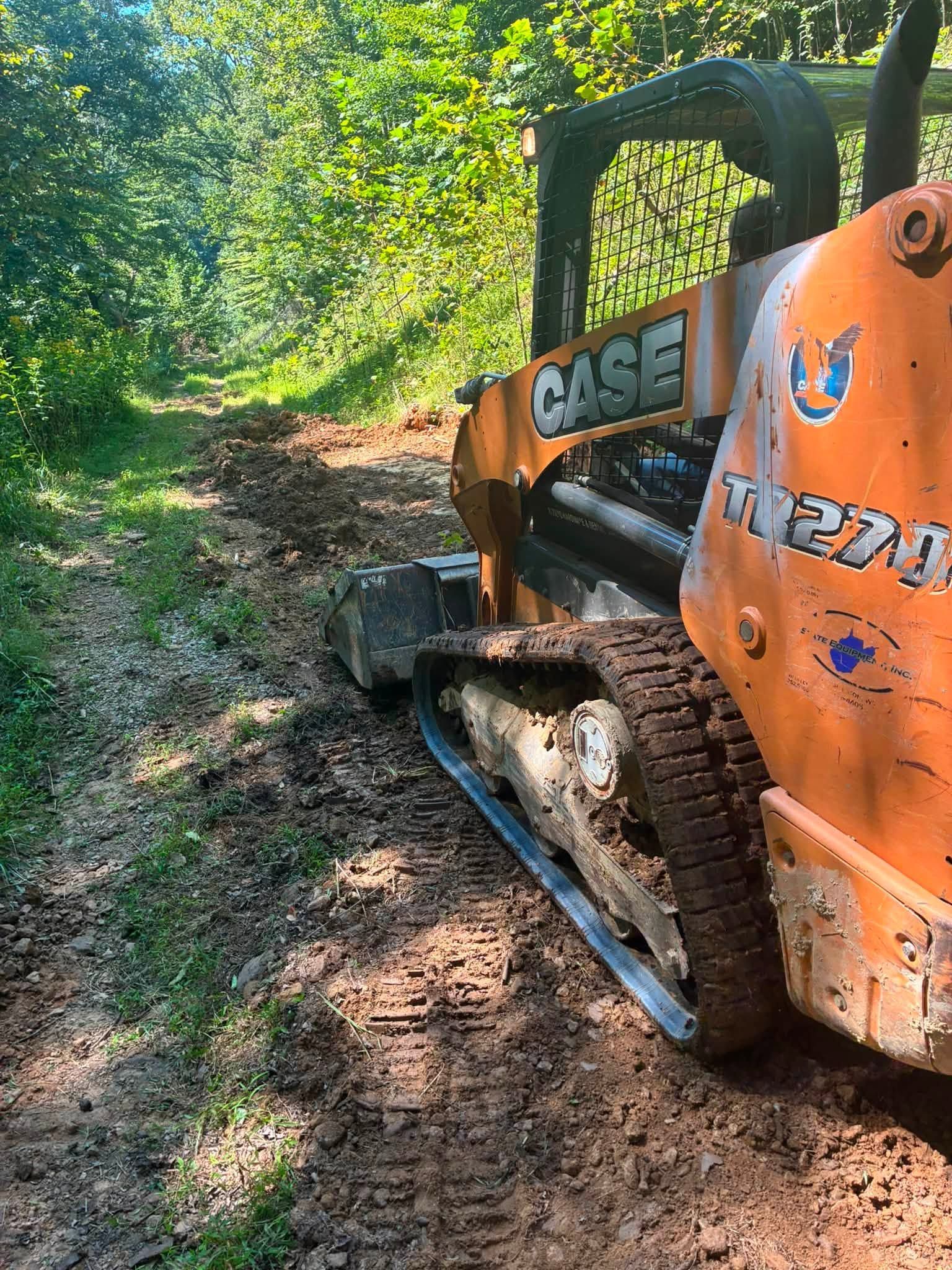 Orange CASE skid steer on a muddy forest trail beside dense green foliage