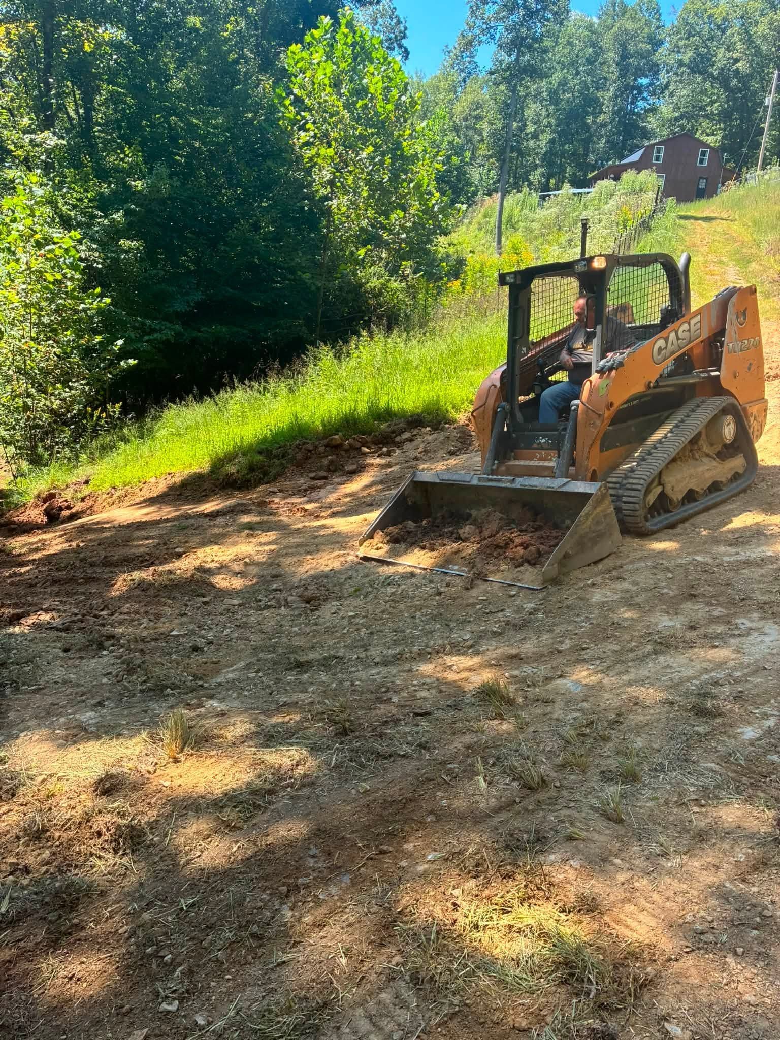 Orange skid steer on a dirt slope in a wooded area, clearing brush in bright sunlight