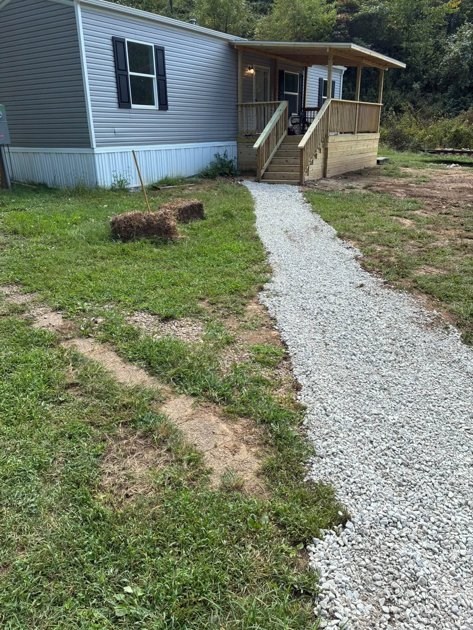 Gray house with a gravel path leading to a front porch and steps, bordered by grass and a tree stump.
