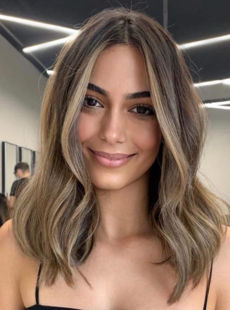 Ritratto di una donna sorridente con capelli mossi e con mèches, in un ambiente interno moderno.