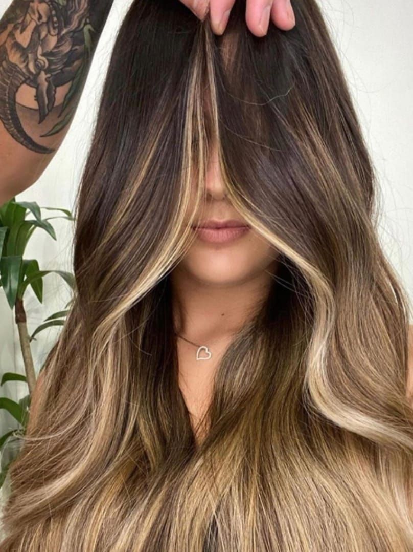 Capelli castano scuro con riflessi biondi, acconciati in morbide onde, tenuti sul viso da una mano
