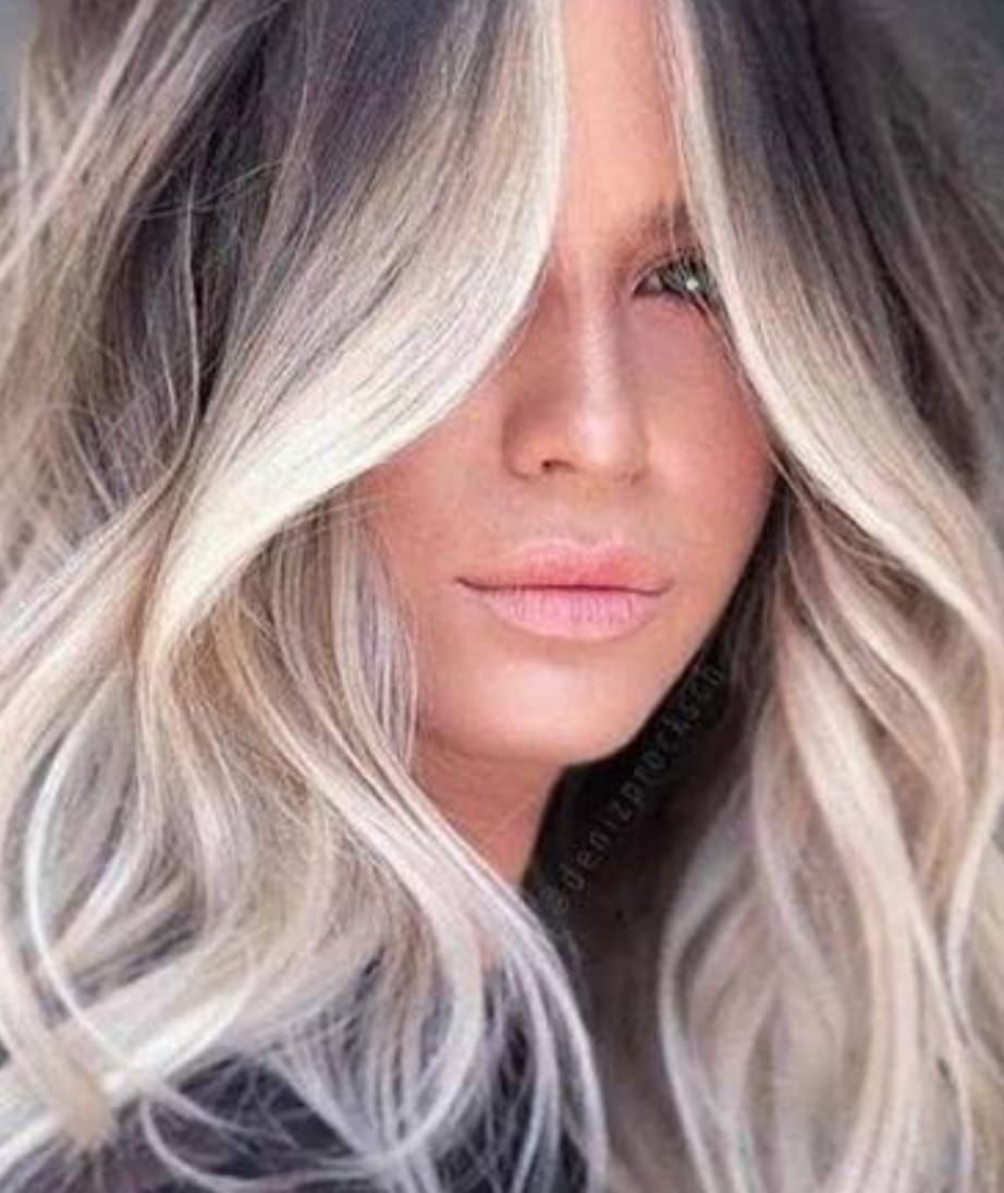 Primo piano di una donna con lunghe onde biondo platino che le coprono parte del viso.