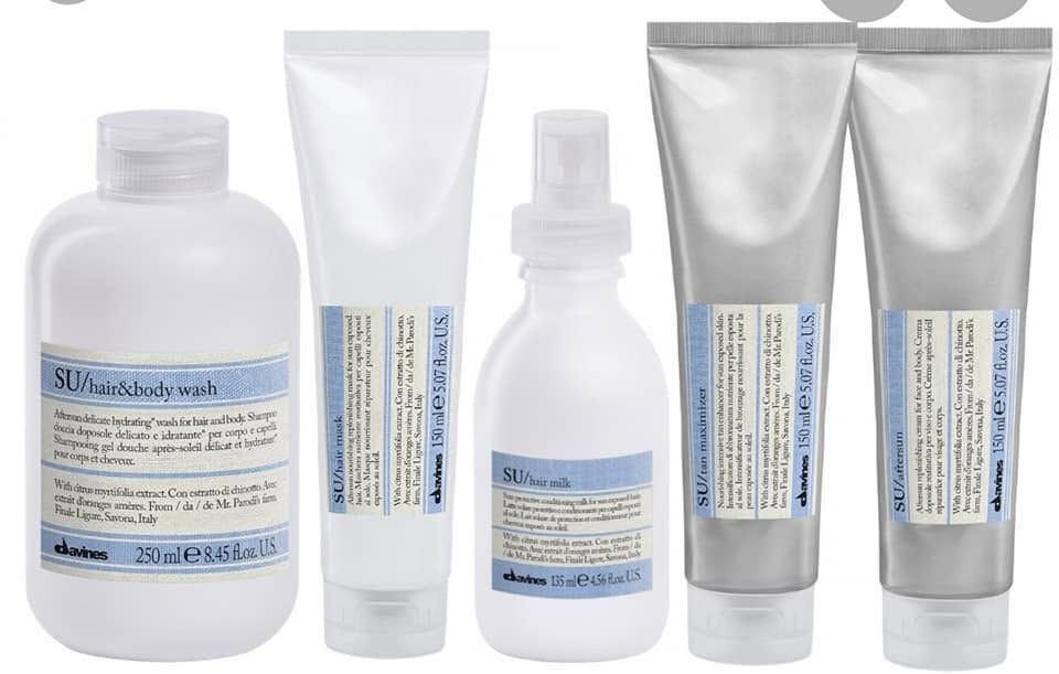 Cinque flaconi e tubetti cosmetici argentati e bianchi allineati su uno sfondo bianco