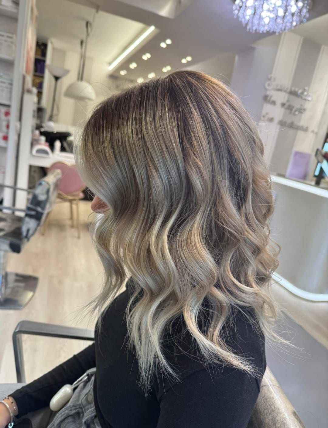 Capelli biondo-castani ondulati di media lunghezza, seduti su una poltrona da parrucchiere, ripresi di spalle e di lato.
