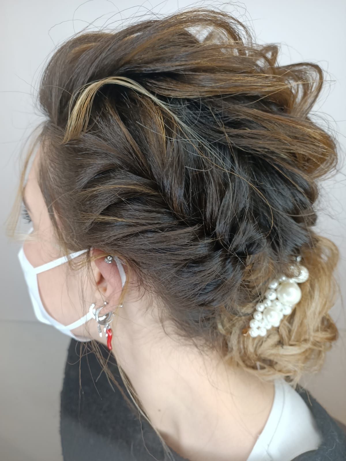Profilo di una persona con un'elegante acconciatura raccolta, che indossa una mascherina bianca e un accessorio per capelli di perle.
