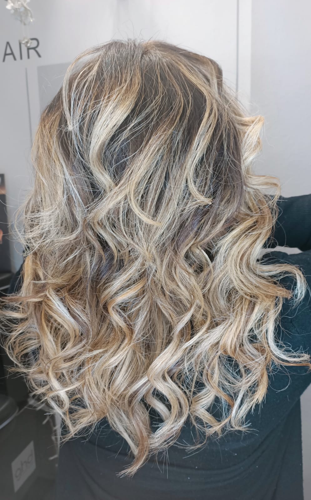 Capelli mossi biondi con mèches castane, acconciati in morbidi ricci, visti da dietro.