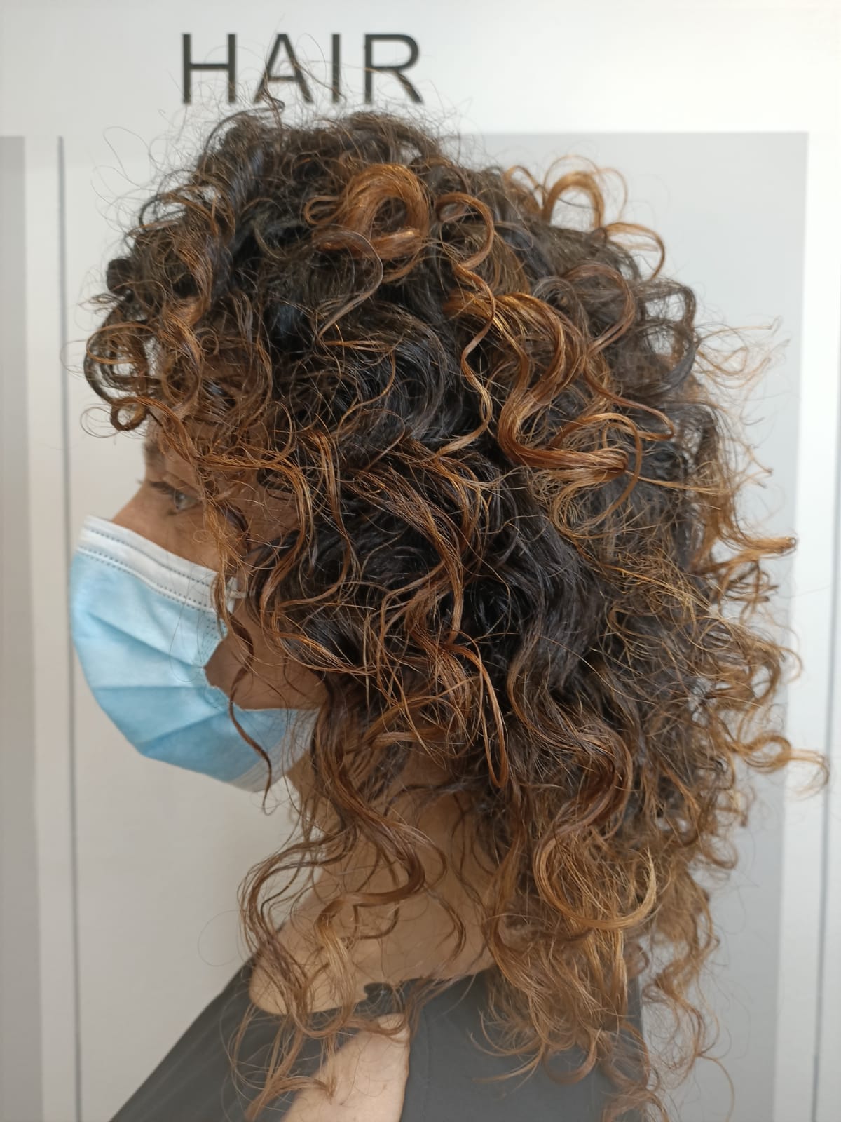 Capelli ricci castani e biondi raccolti in un'acconciatura voluminosa, vista laterale con mascherina blu.