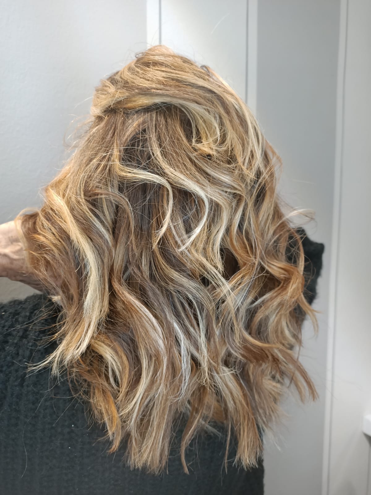 Capelli biondi ondulati di media lunghezza con radici scure, raccolti in una mezza coda morbida con torsione.