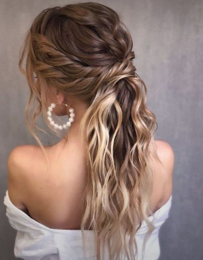 Elegante acconciatura semi-raccolta con trecce, capelli biondi mossi e sciolti e orecchini a cerchio di perle, vista da dietro.