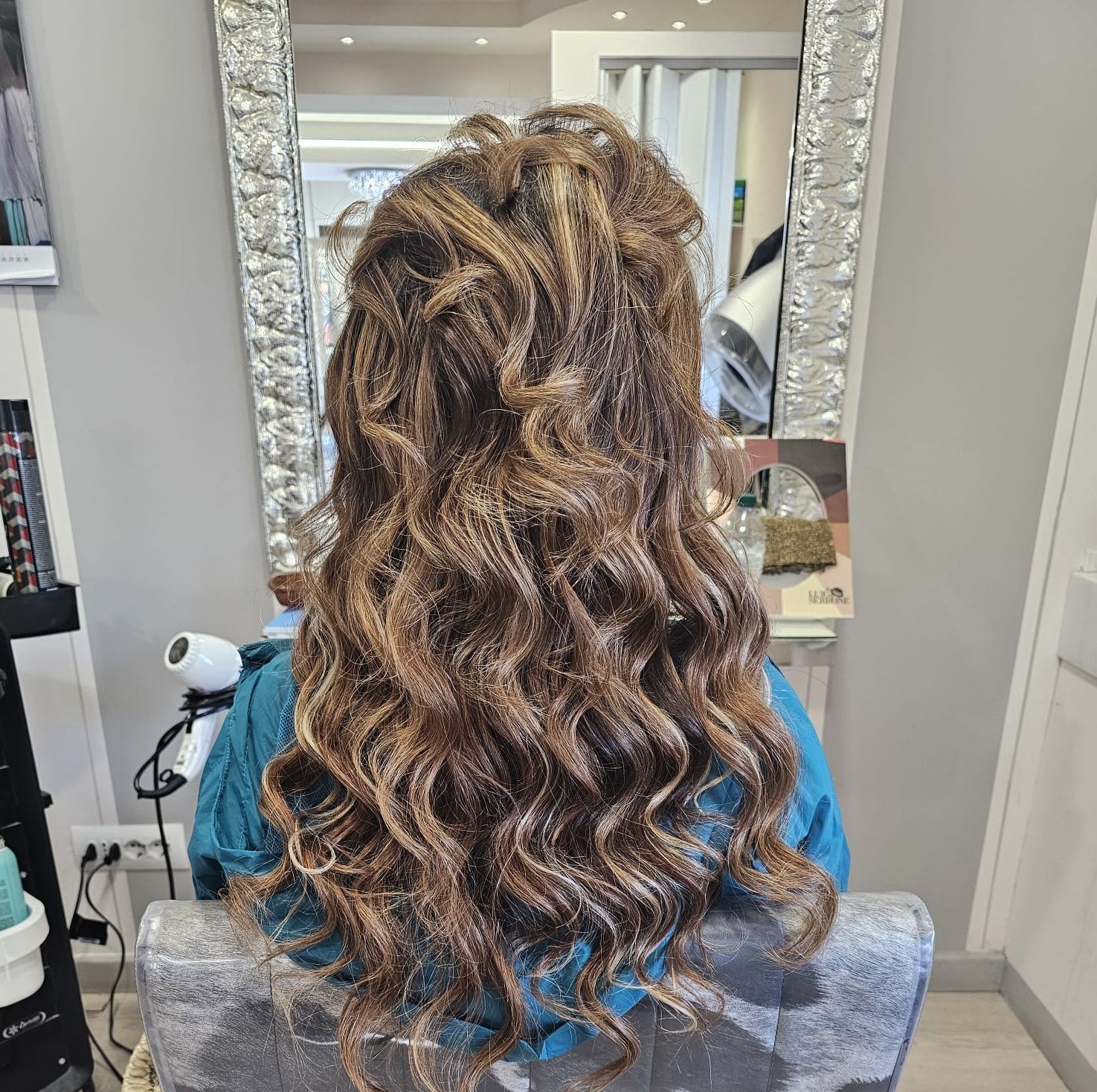 Lunghi capelli castani ricci acconciati su una poltrona da parrucchiere, visti da dietro.