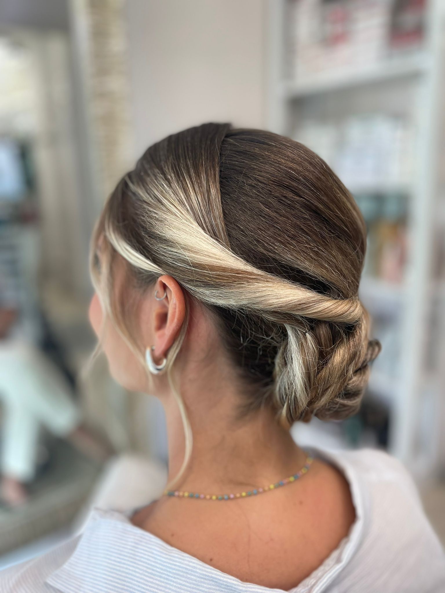 Acconciatura raccolta con trecce, capelli scuri e mèches bionde, vista da dietro in un salone di bellezza.
