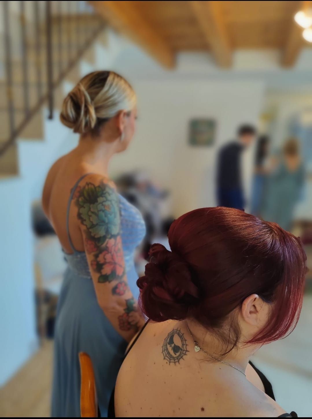 Due persone tatuate sedute in uno studio al chiuso con luci soffuse, una delle quali in primo piano con i capelli rossi a fuoco.