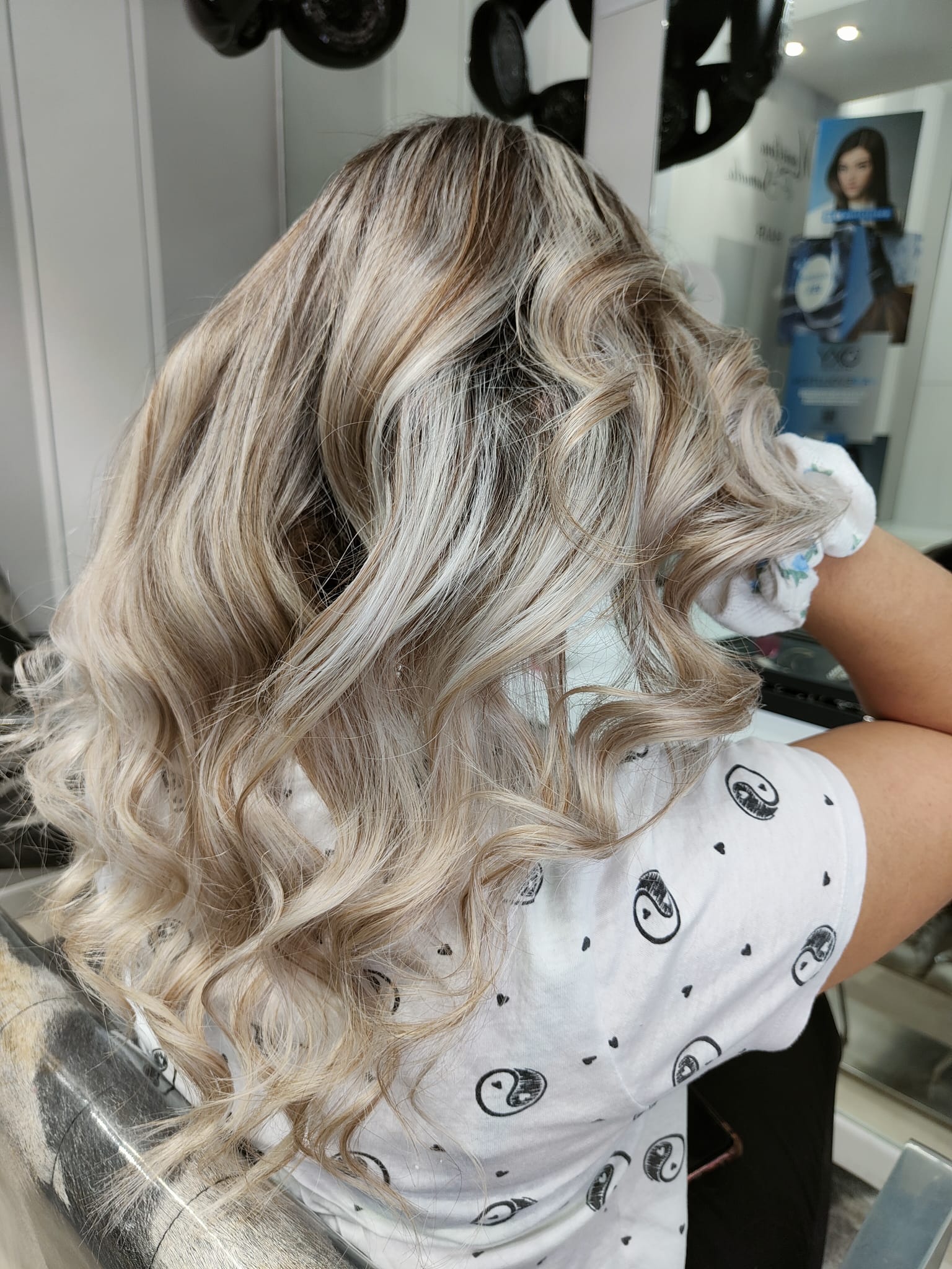 Capelli biondi ondulati con radici scure, visti di spalle da una poltrona da parrucchiere.