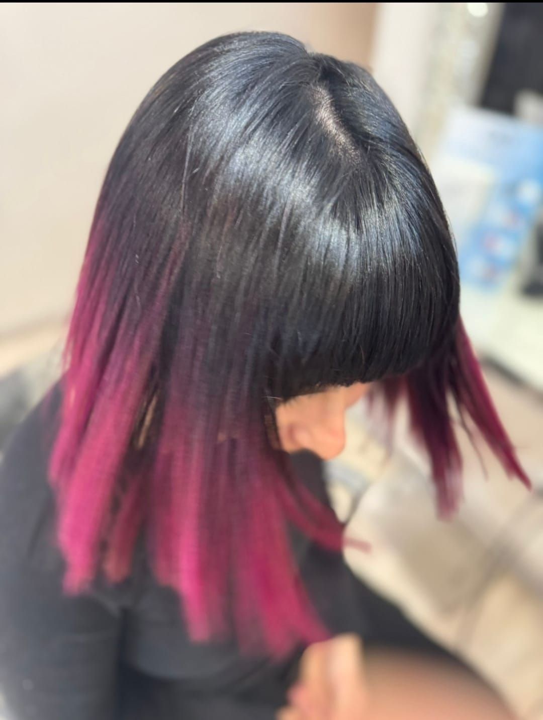 Caschetto nero con punte sfumate rosa acceso, fotografato di profilo in un salone.