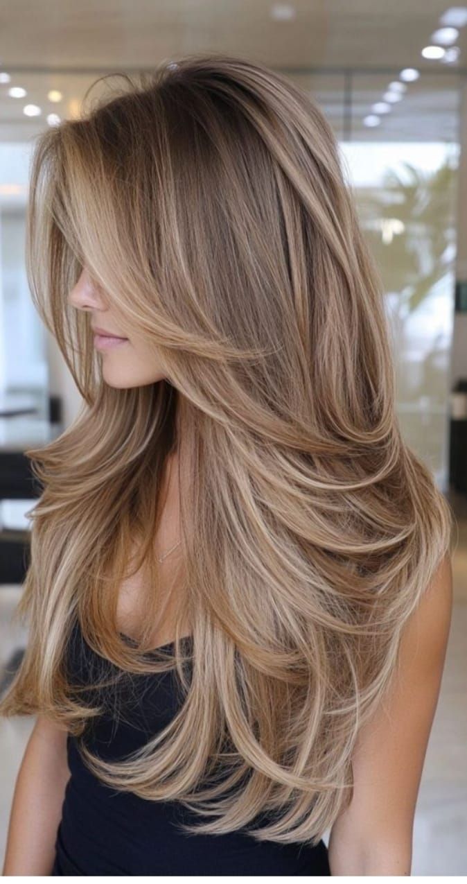 Donna con lunghi capelli biondi scalati, con indosso una maglietta nera, ritratta di profilo in un ambiente interno.
