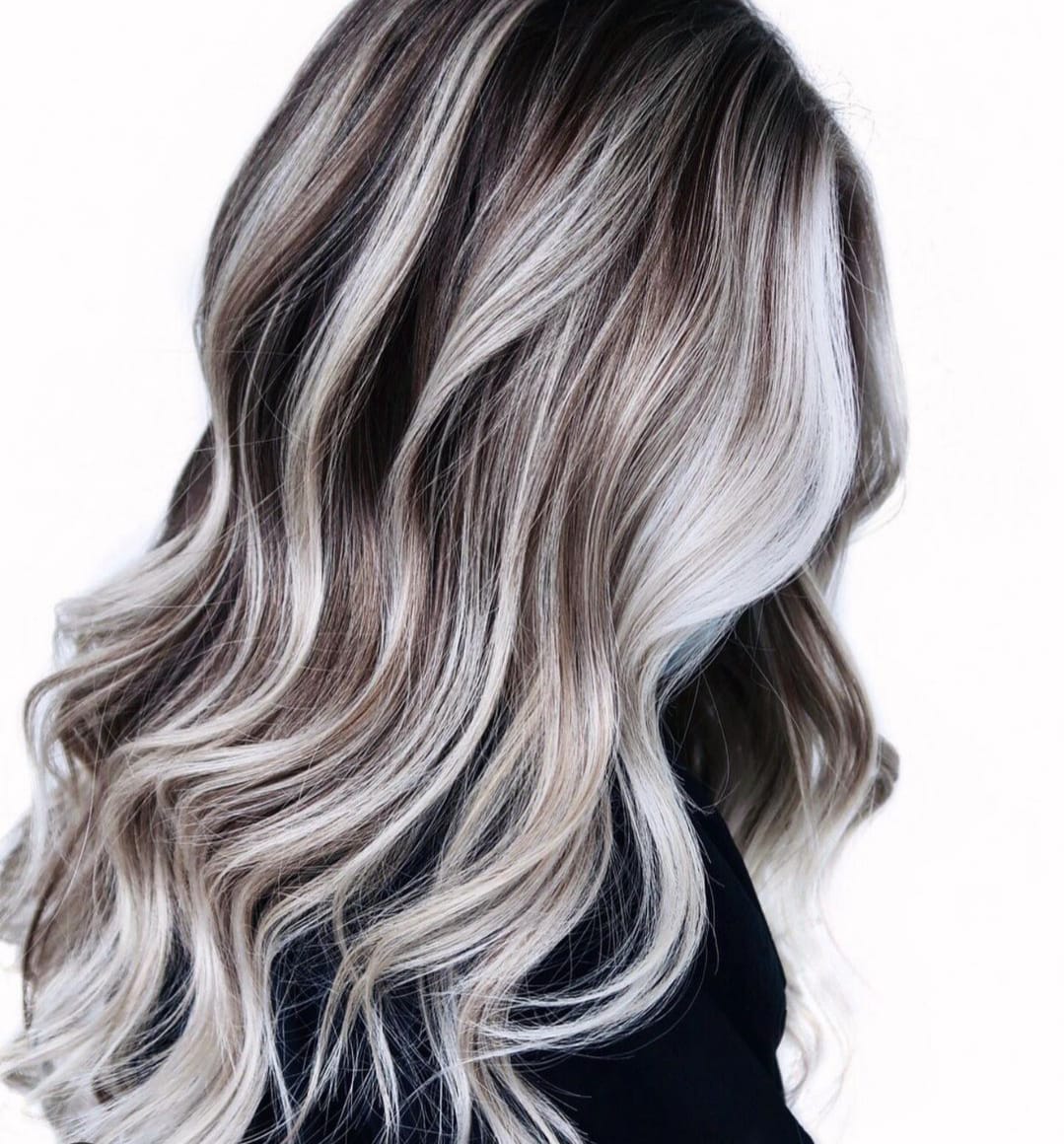 Lunghi capelli mossi biondo platino con radici scure, mostrati di profilo su una persona con una maglietta nera