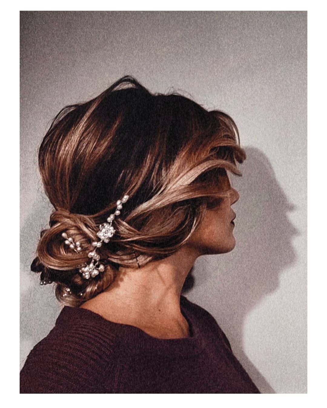 Vista laterale di una persona con capelli castani raccolti in un'elegante acconciatura, ornata da fermagli di perle e fiori.