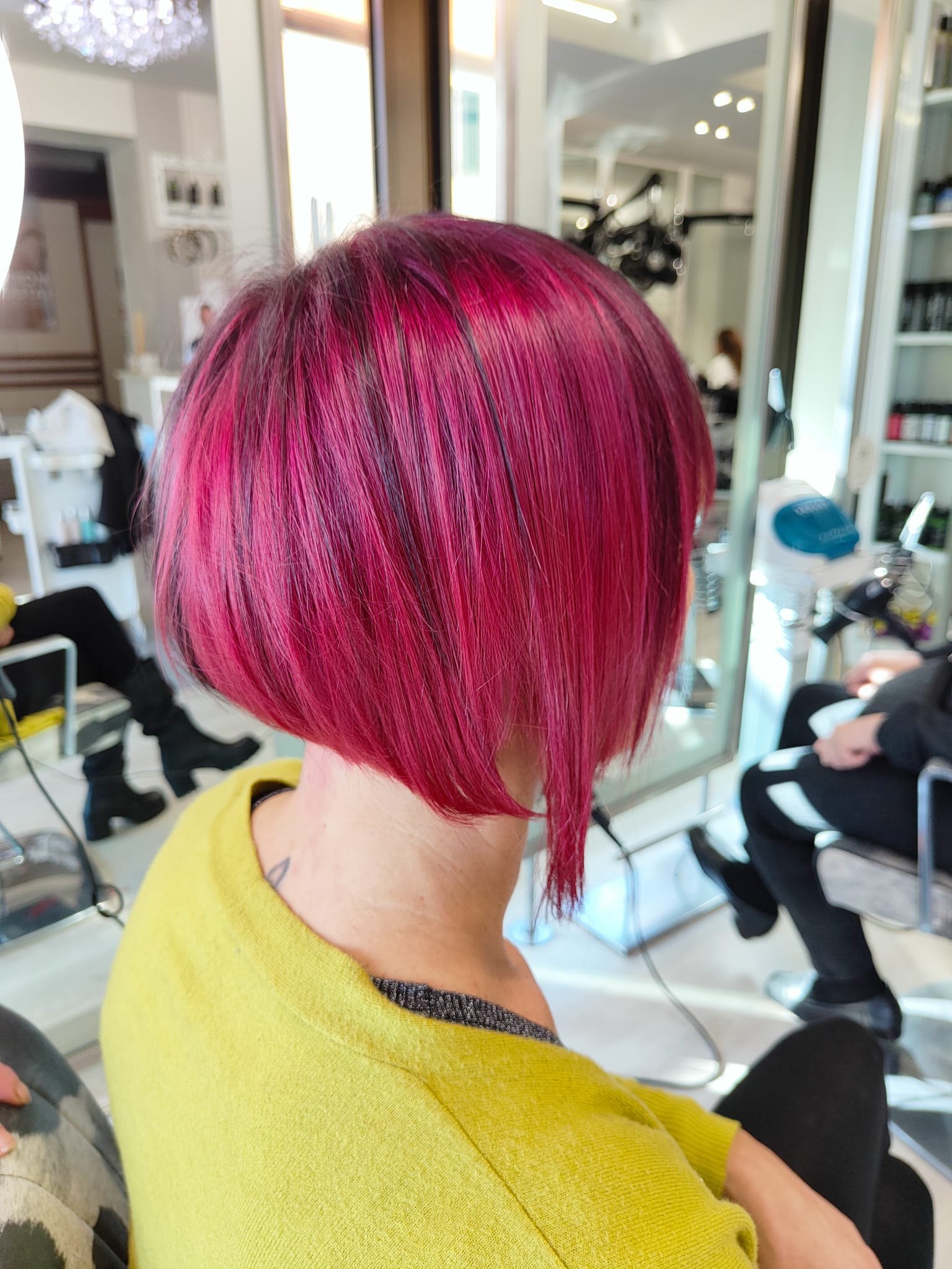 Persona con caschetto asimmetrico rosa acceso seduta su una poltrona da parrucchiere, vista da dietro.