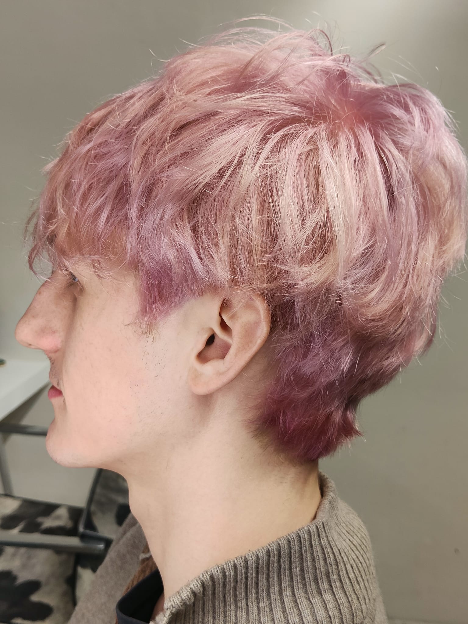 Profilo laterale di una persona con capelli corti rosa su uno sfondo interno neutro.