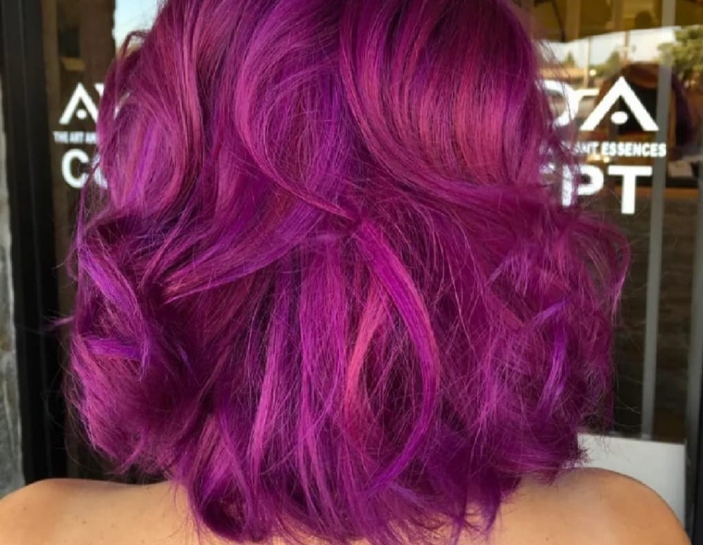 Vista posteriore di capelli mossi di media lunghezza, tinti di un vivace color magenta-violaceo, in un salone di bellezza.