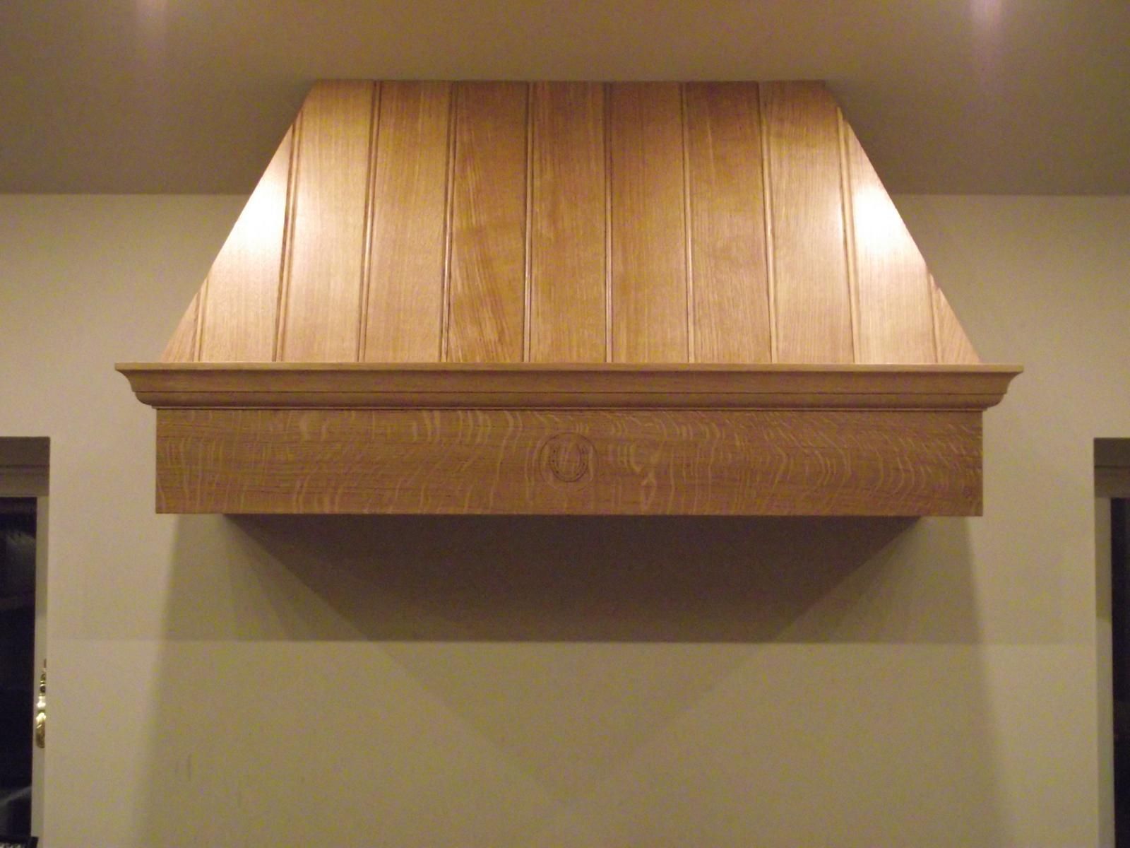 A wooden hood is hanging from the ceiling in a kitchen