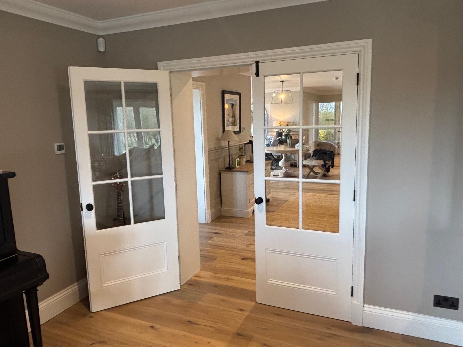 A living room with hardwood floors and white doors leading to a living room.