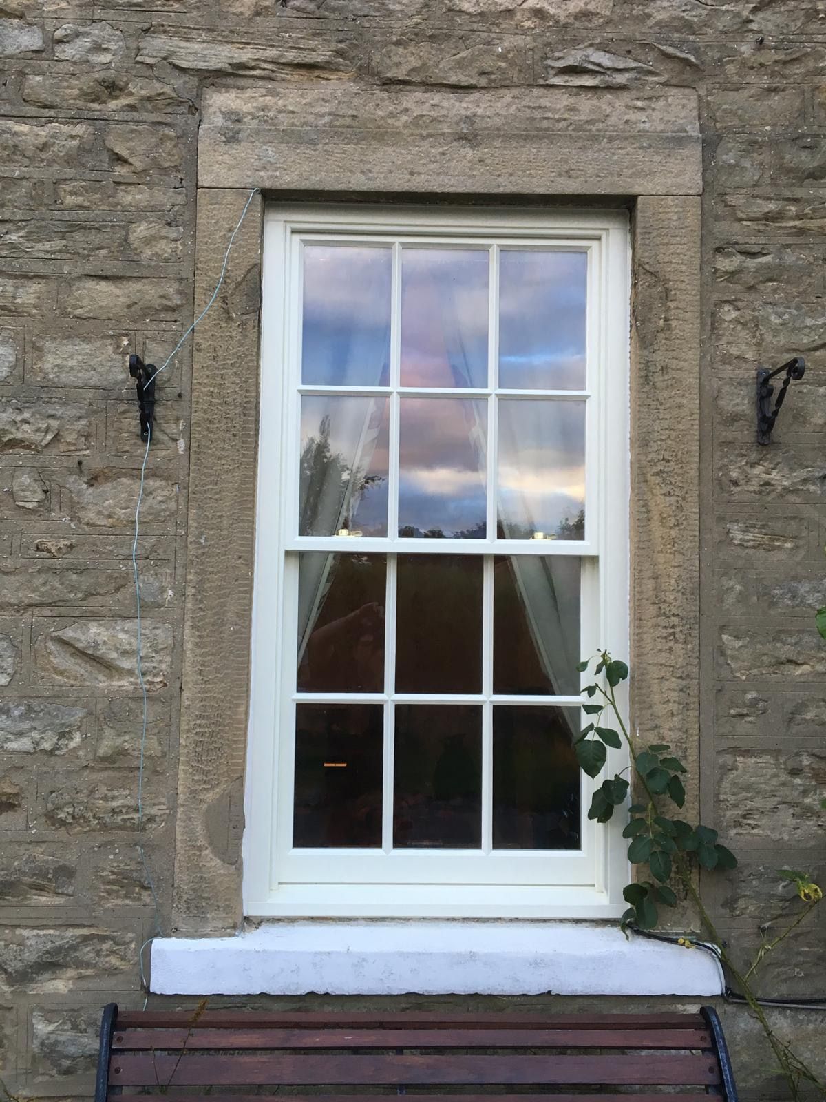 A white window is on the side of a stone building.