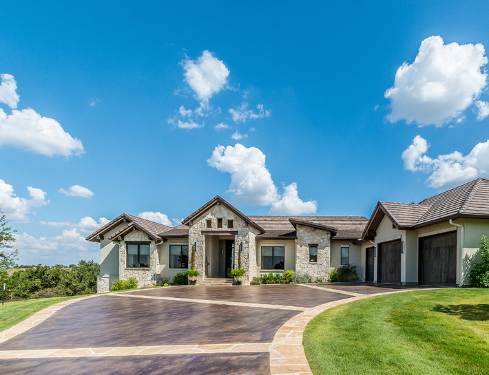 Exterior of a stone house with a brown concrete driveway, on a sunny day.