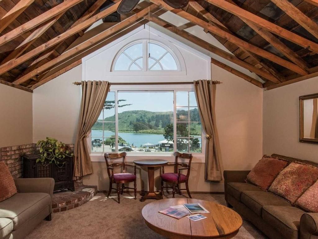 Living room with a lake view, exposed wooden ceiling beams, fireplace, sofa, chairs, and round coffee table.