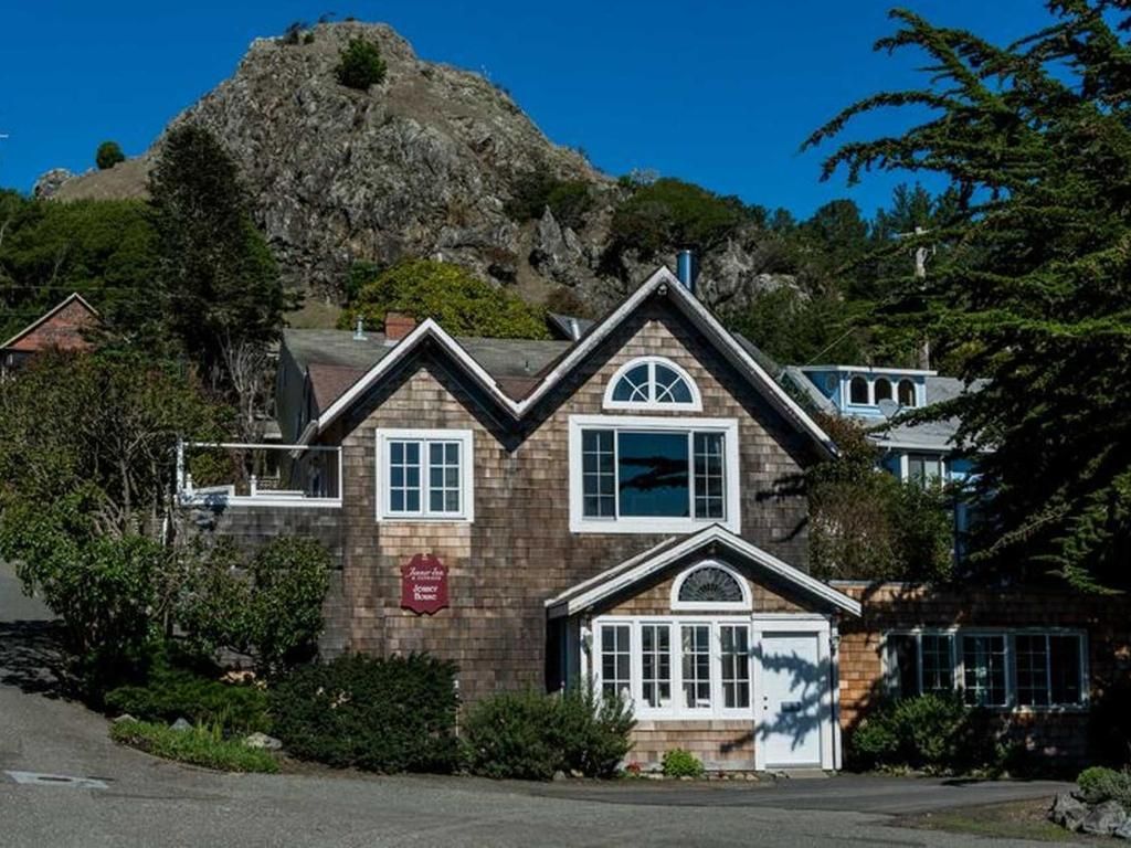 Brown shingled house with white trim, set against a rocky hill under a blue sky.