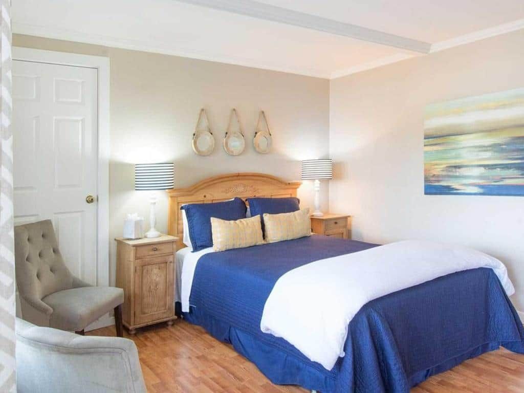 Bedroom with blue bedspread, nightstands, and wall art. Features light-colored wood floor and a chair.