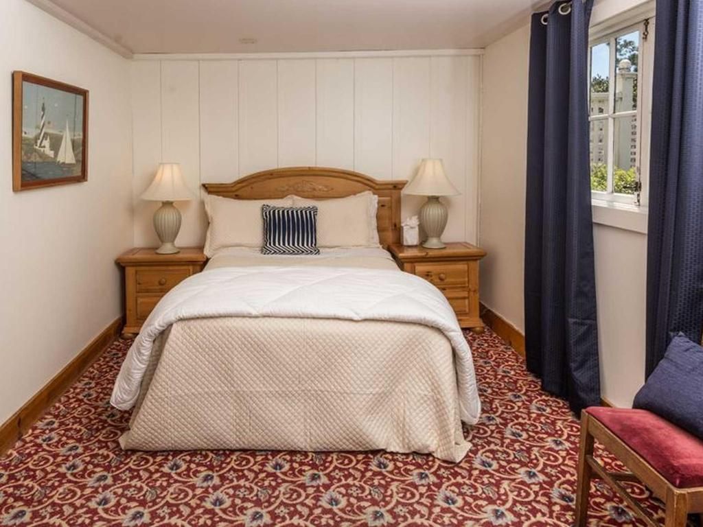 Bedroom with a bed, nightstands, lamps, window, and patterned red rug.
