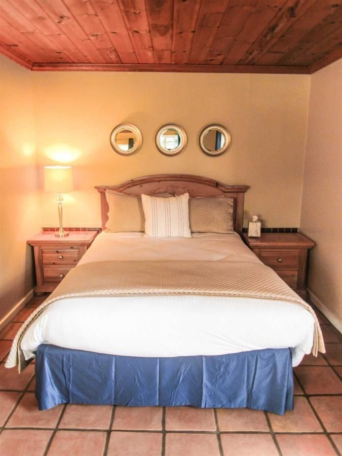 Bedroom with a wooden headboard, beige bedding, blue bed skirt, wooden nightstands, and three round mirrors.