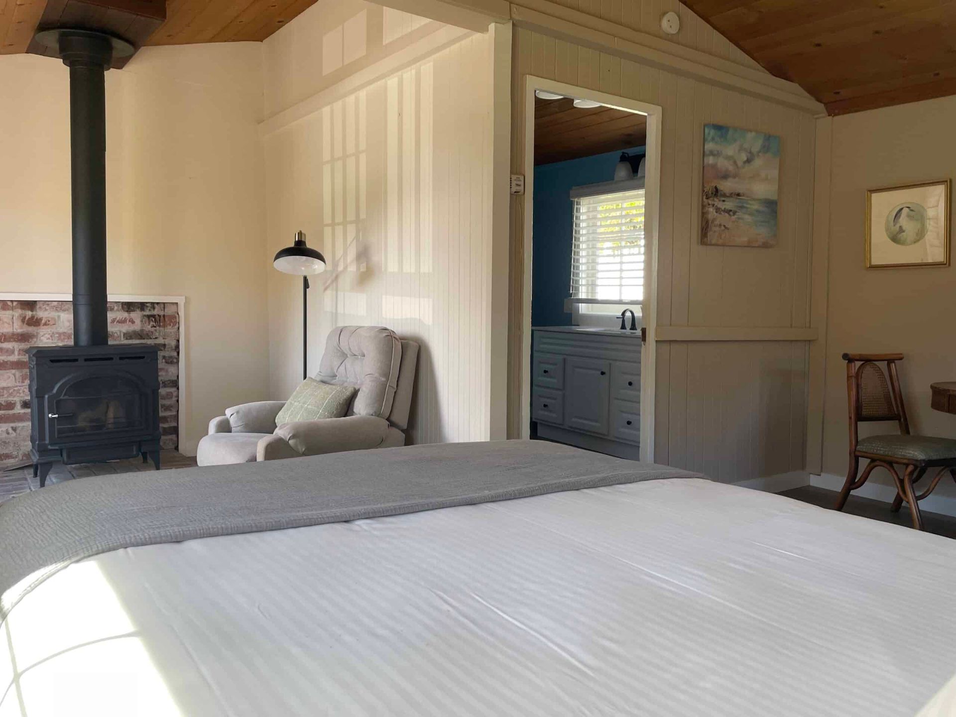 Cozy cabin bedroom with a fireplace, armchair, and open doorway to a bathroom.