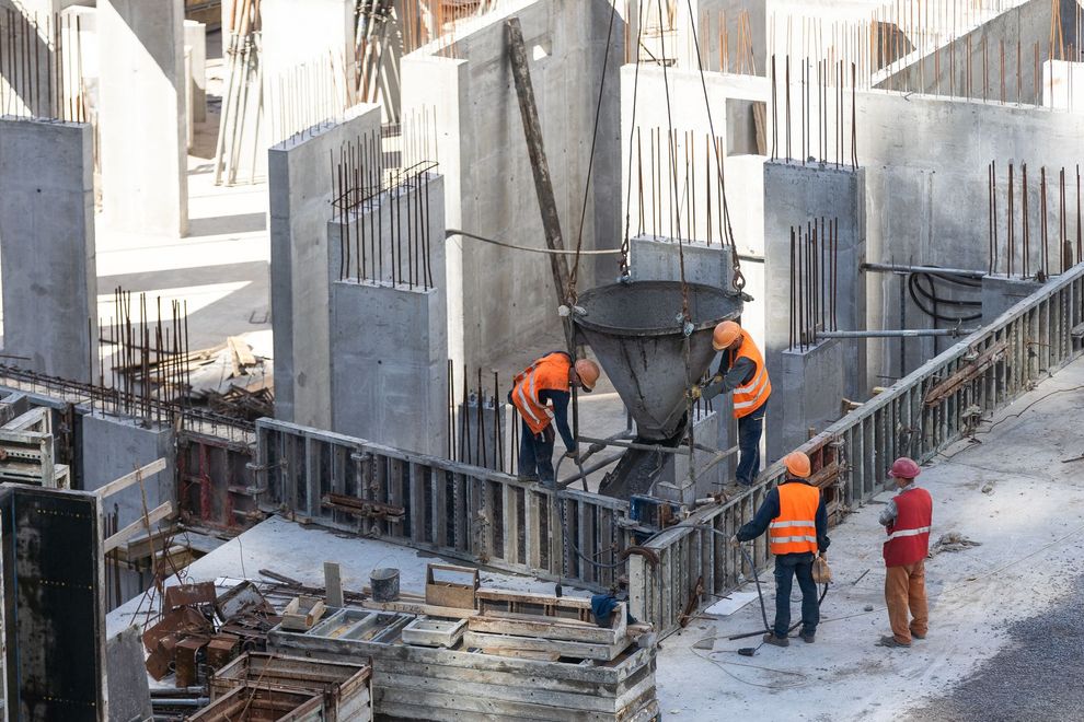 Construction workers in orange vests pouring concrete at a building site