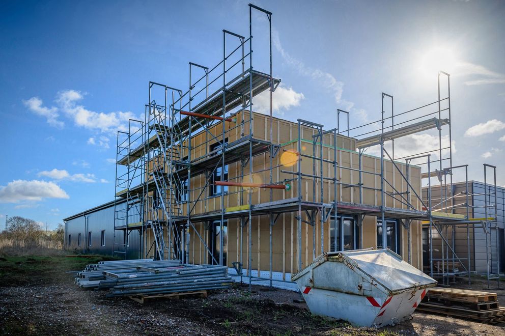 Scaffolding around a house under construction, with stacks of lumber and a cloudy blue sky.