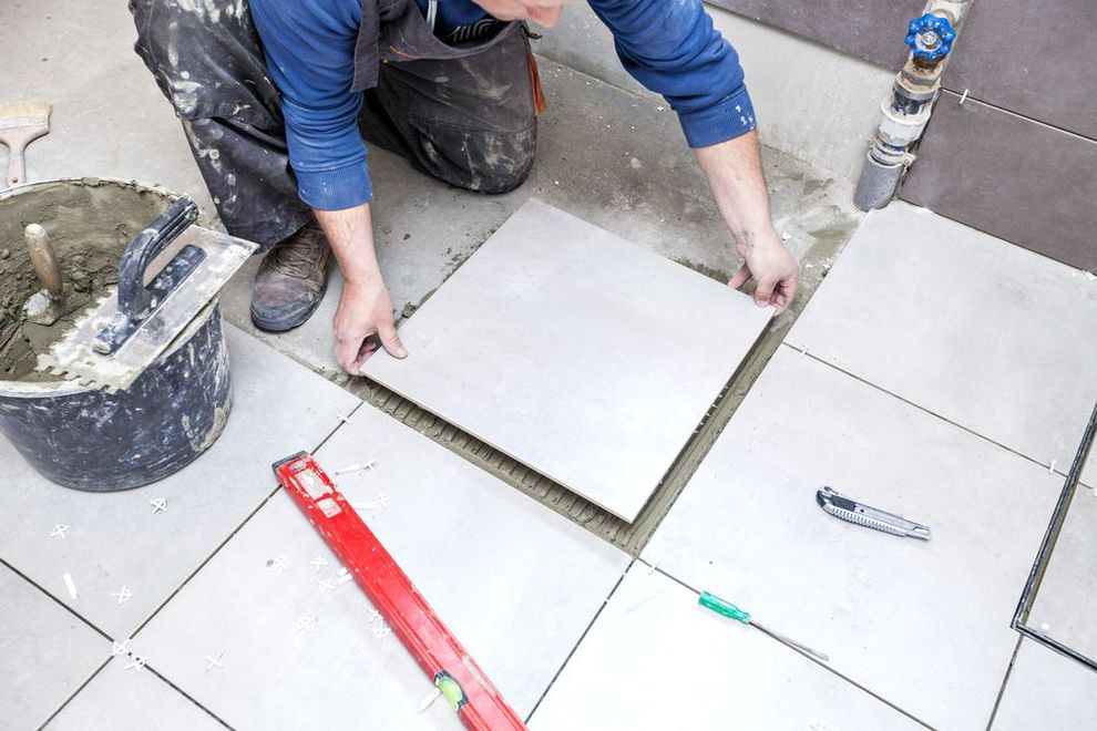 Worker laying large gray tiles on an outdoor patio with a red level tool nearby