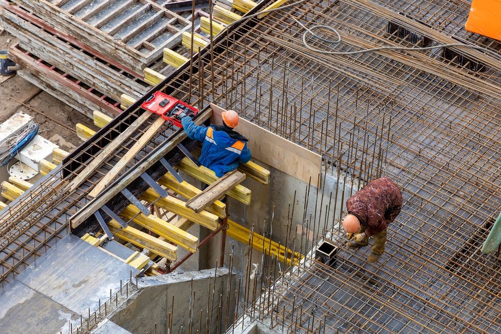 Workers tying rebar at a construction site with scaffolding and concrete forms
