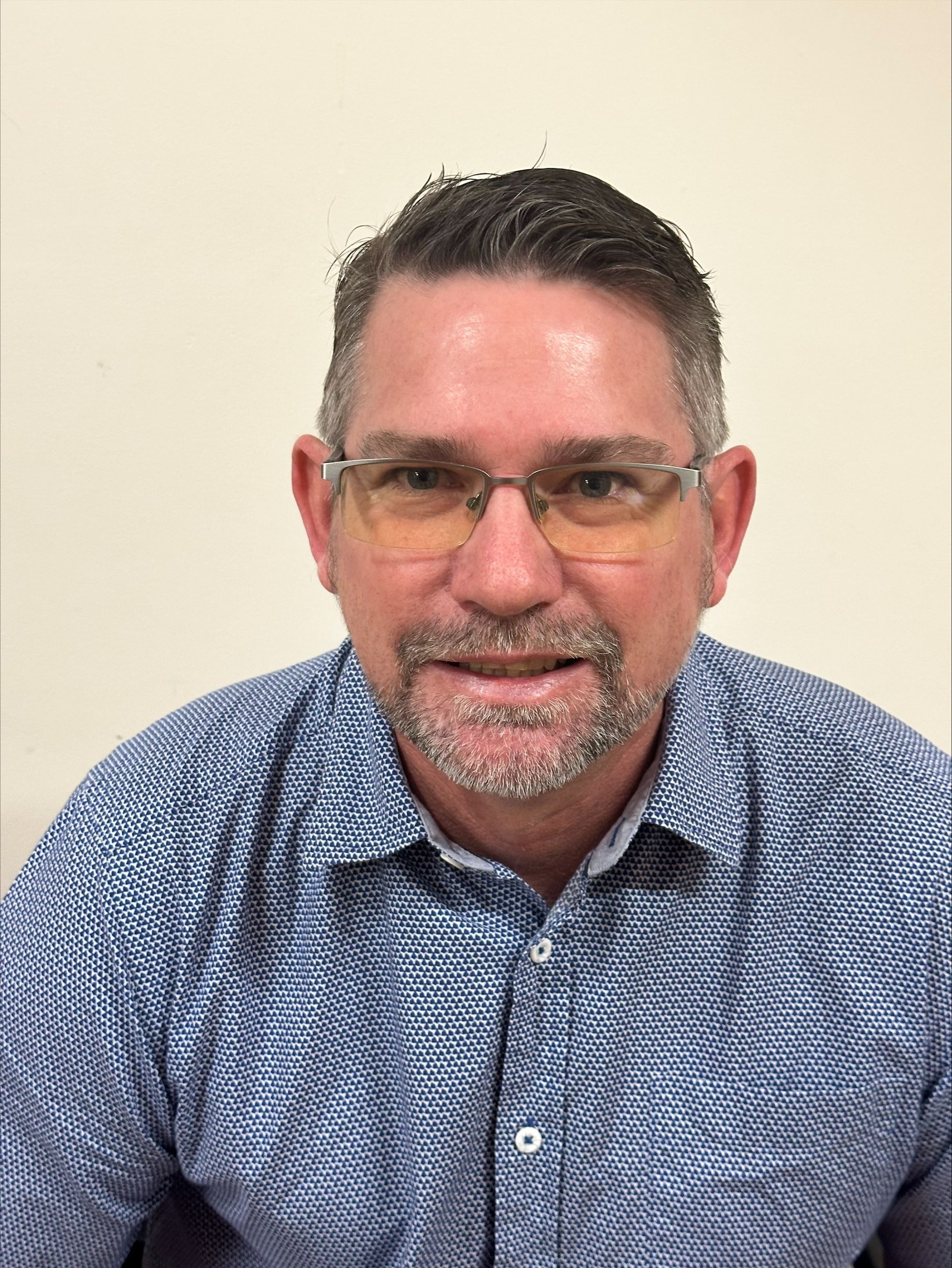A man with glasses and a beard is wearing a blue shirt.