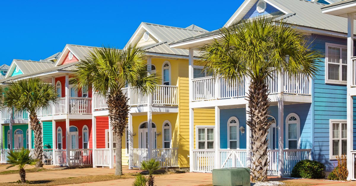 Colorful beachside row of pastel houses with white porches and palm trees under a bright sky