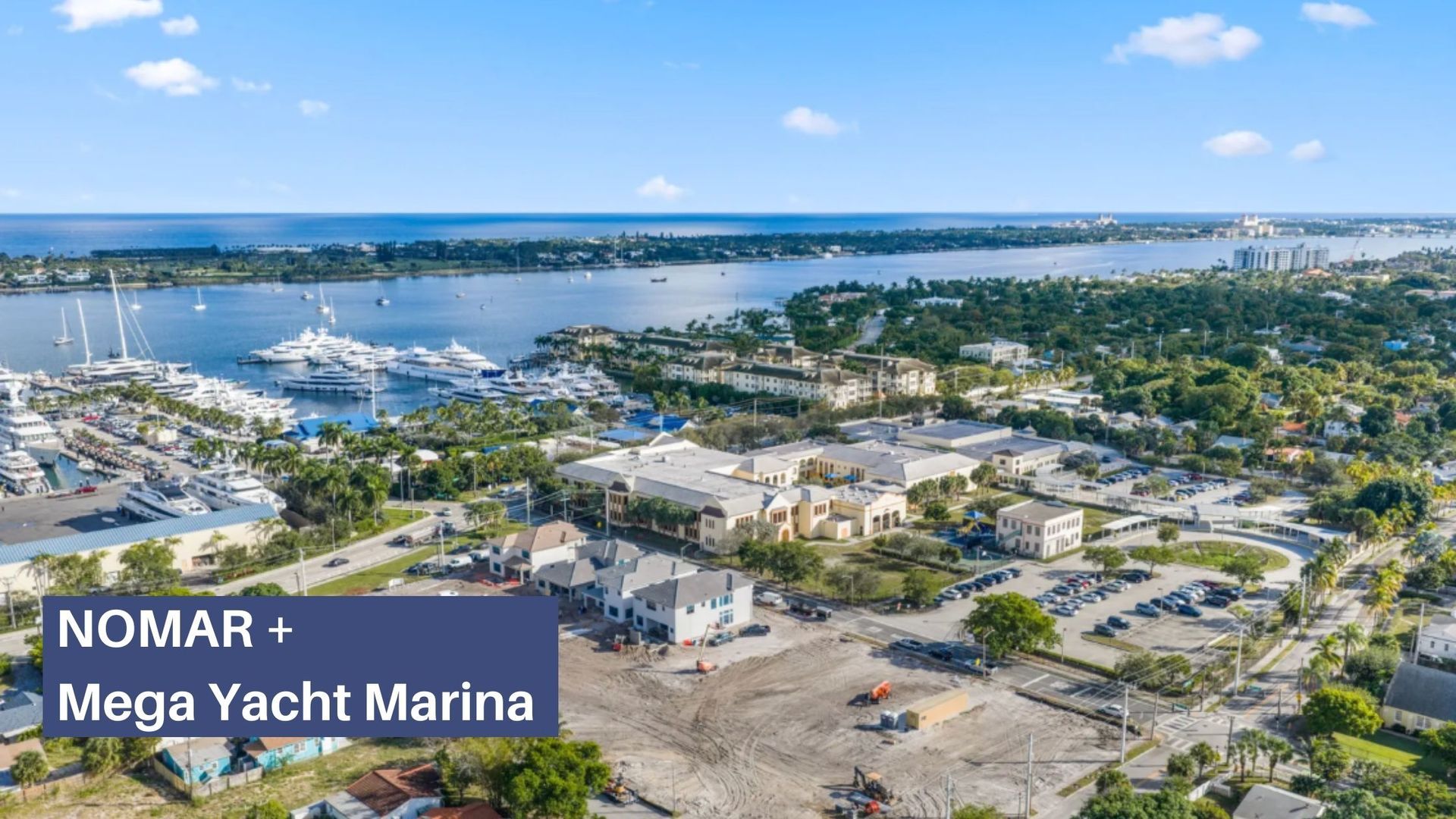 Aerial view of a marina with yachts, waterfront buildings, and blue water under a clear sky