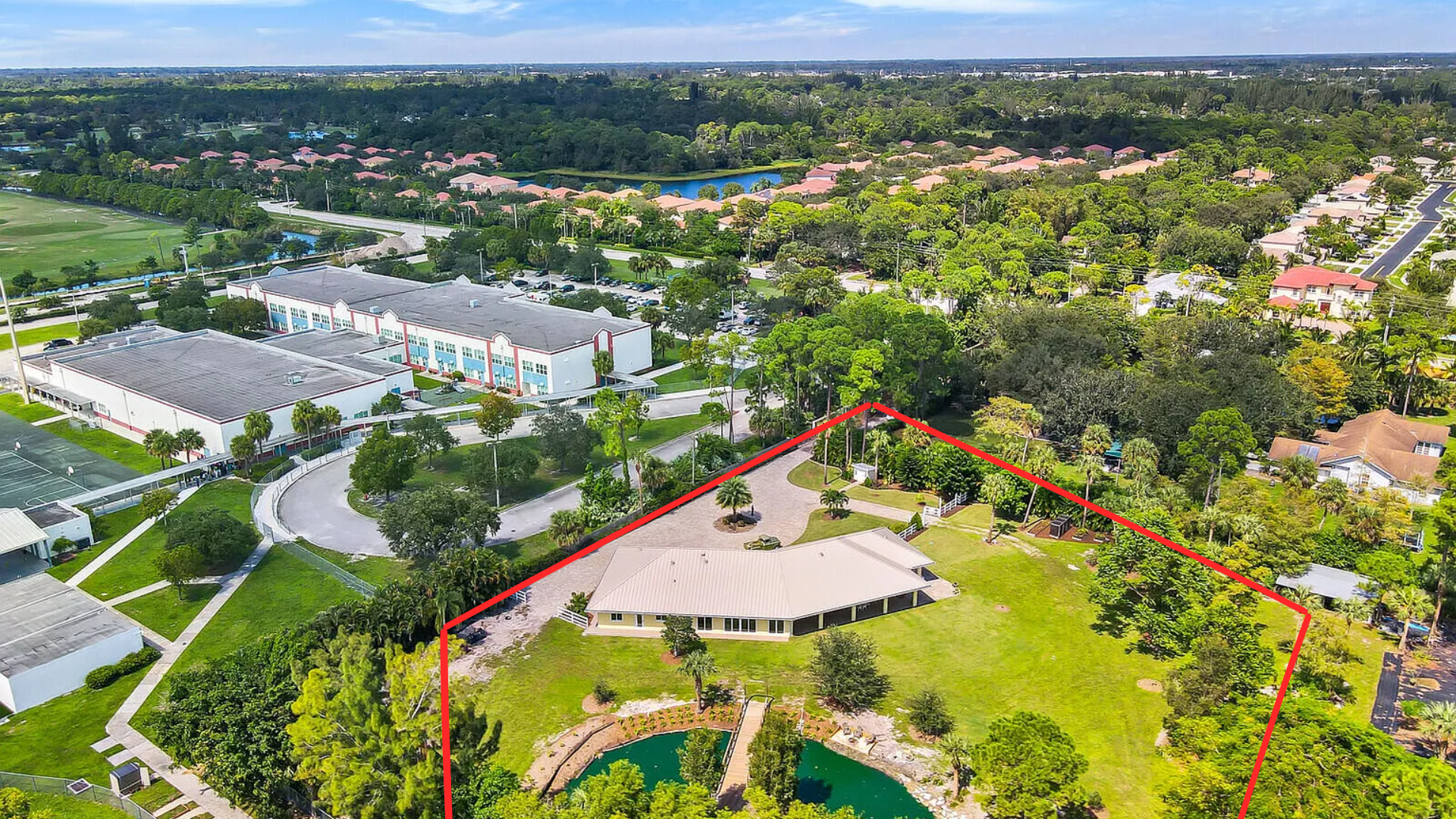 Aerial view of a large park with a red boundary, paths, trees, and nearby buildings under clear skies