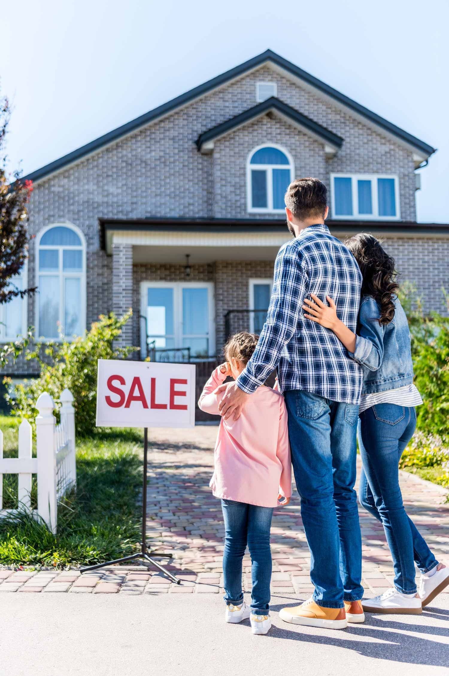 Family standing in front of a house for sale sign
