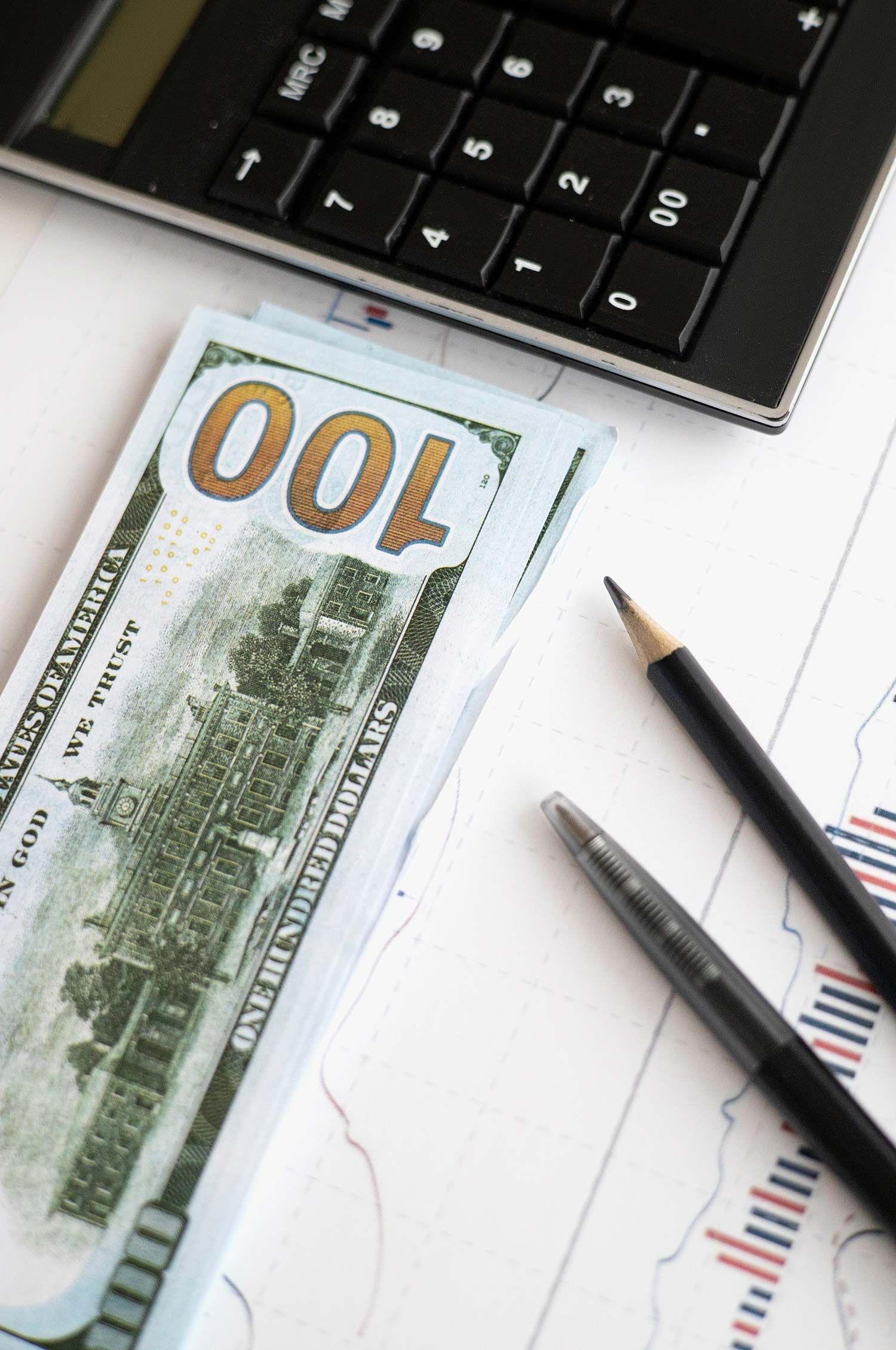 Cash and pencil beside a laptop on a desk with financial charts