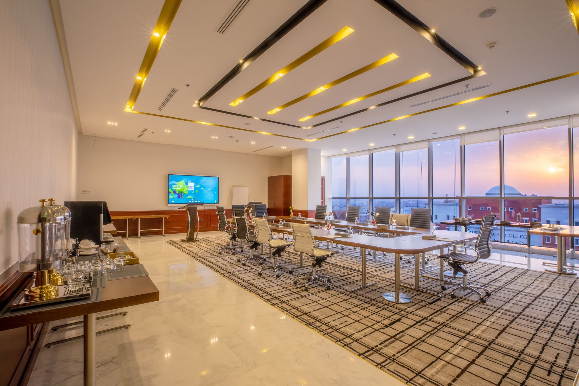 Modern conference room with tables, chairs, large windows, and a sunset view over water