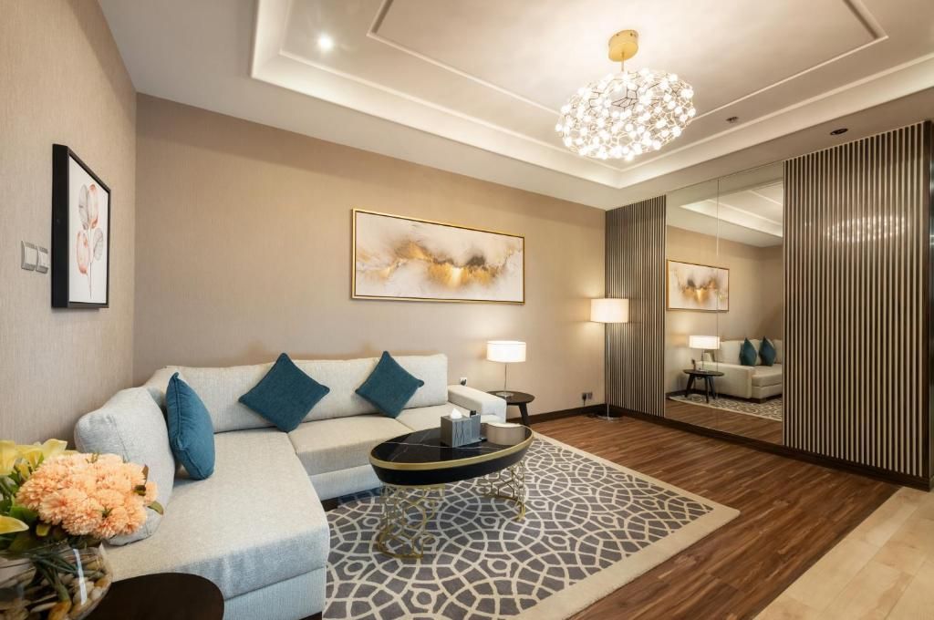 Elegant living room with beige sofa, blue pillows, patterned rug, chandelier, and mirrored wall