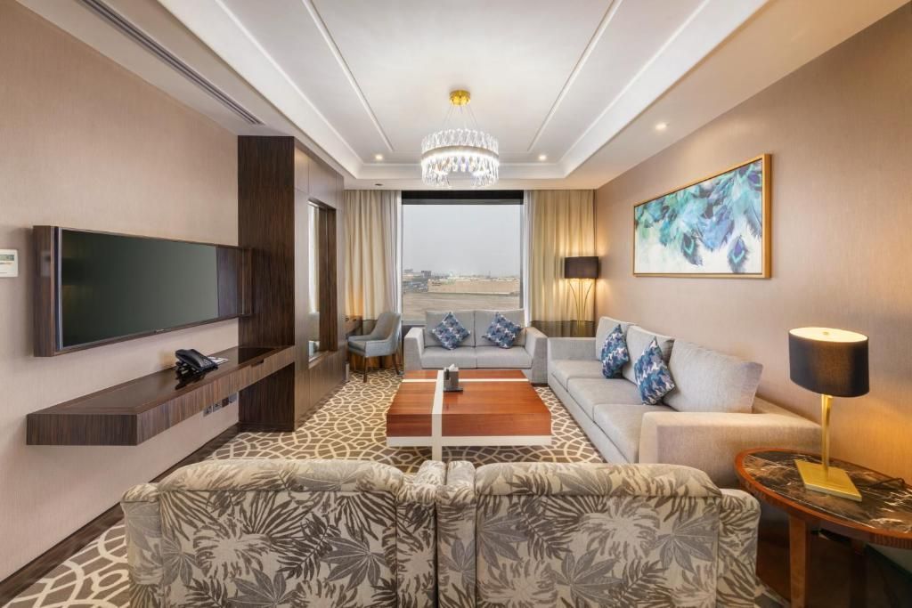 Modern hotel suite with sofa, TV, coffee table, chandelier, and large window view