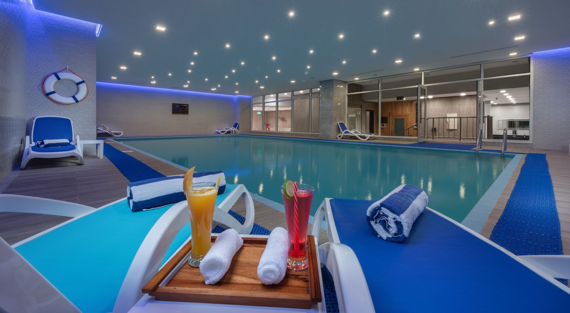 Indoor swimming pool with blue and white accents, lounge chairs, drinks, and a life preserver.